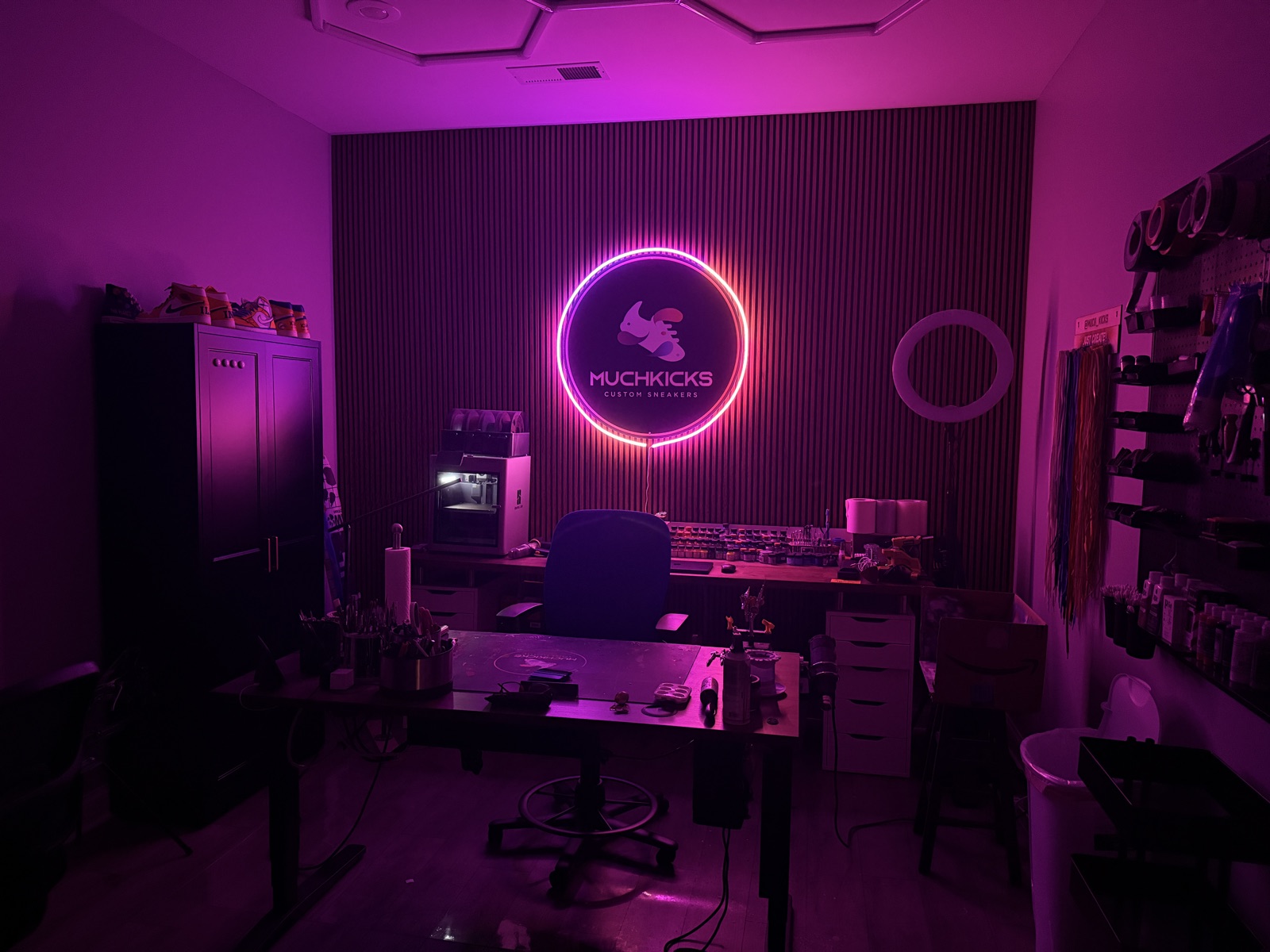 The Muchkicks studio — paint bench, lacing wall, and lit logo sign